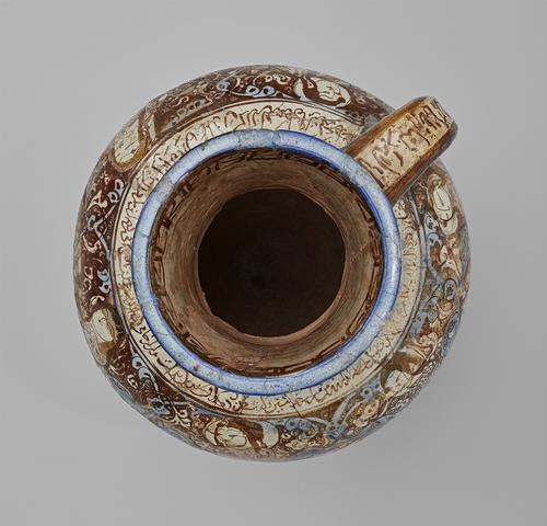 Top view of a ceramic jug with a slender handle, bulbous lower body, and rimmed opening. Decorated with brown and blue against a white body, showing figures and bands of inscriptions. The rim is coloured blue, and there is a band of decoration inside the mouth of the jug.