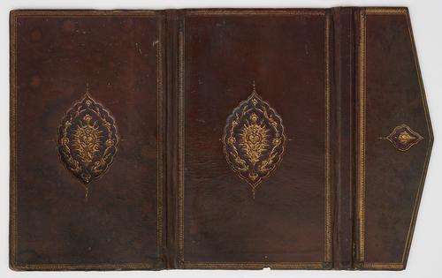 Outside cover of dark brown leather bookbinding, laid flat with envelope flap on the right. Spine appears creased and worn. Both covers feature identical embossed golden oval medallion motif in the centre. Envelope flap has similar smaller motif. Faded golden coiled border lines each cover and envelope flap.