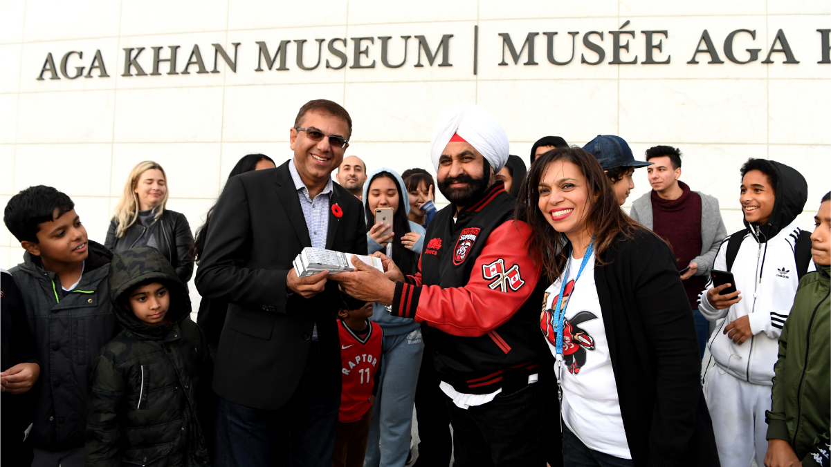 Museum CEO Moyez Jadavji accepts a bundle of tickets from Nav Bhatia, outside the Museum, surrounded by children.