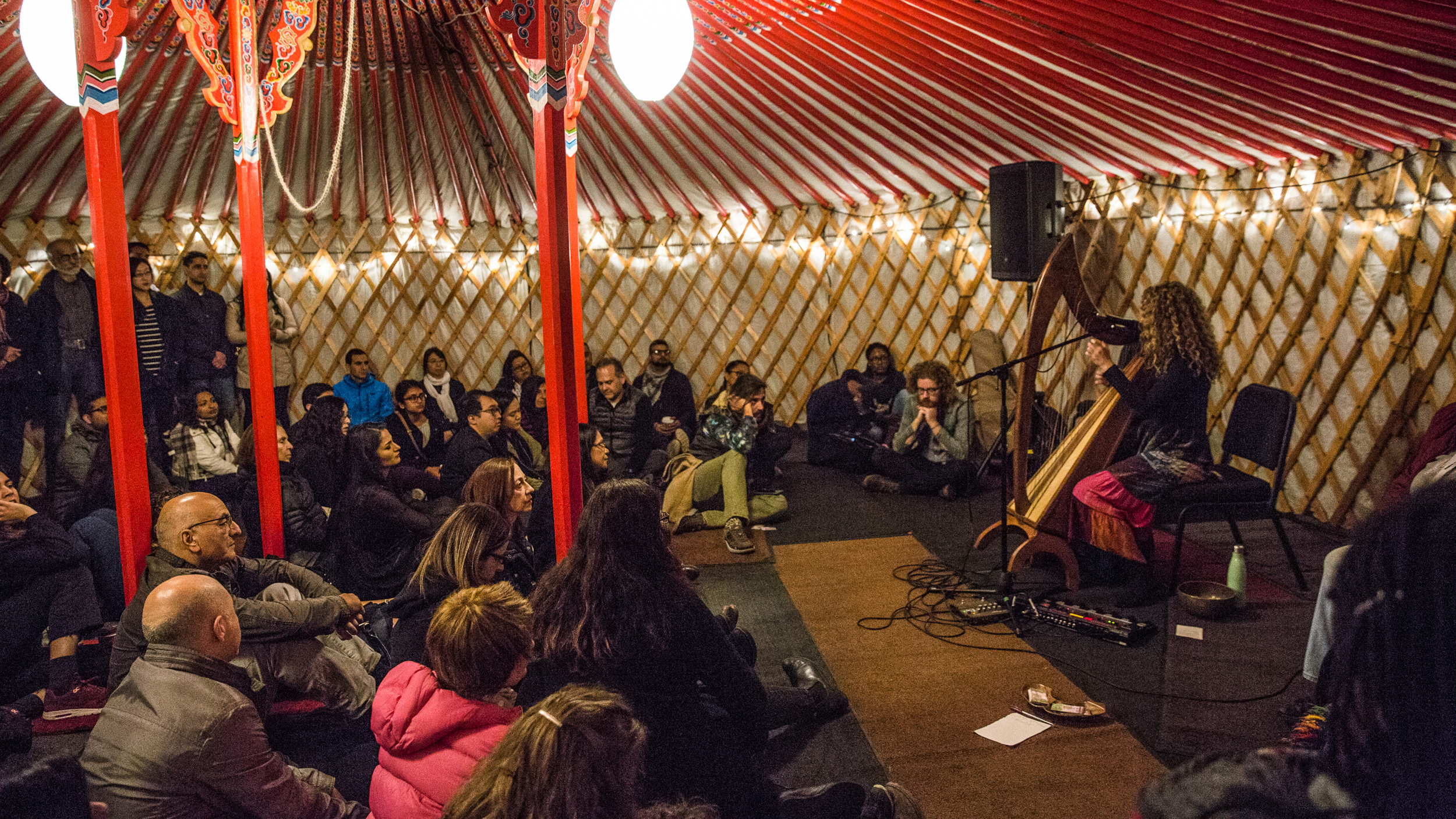 Spectators sitting on the floor enjoy the music of a harp player inside a Mongolian yurt.