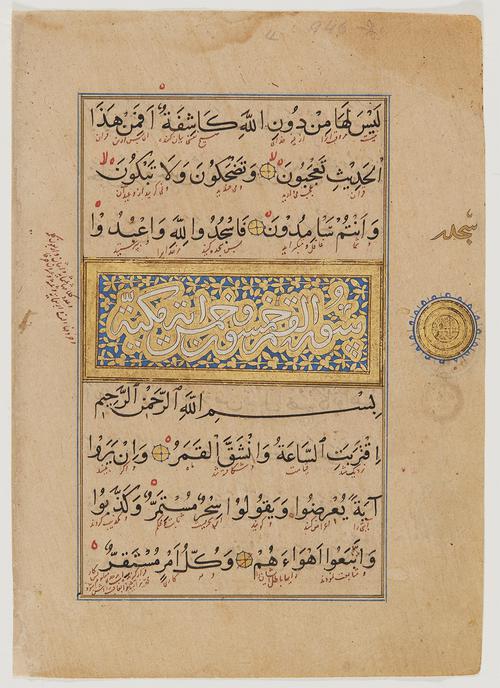 Page with 7 lines of black text, annotated in red ink and accented by four small gold circles. Three lines down is an illuminated panel with white script decorated with golden vines on a blue background. In the right margin, above a gilt medallion, there is a gold annotation.