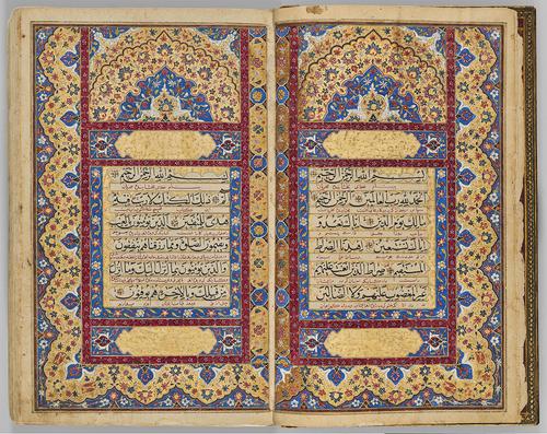 Book opened to a highly illuminated frontispiece double page spread. Text boxes on each page are in the centre surrounded by highlight decorated boarders. Boarders of blue, gold, burgundy, and white floral pattern.