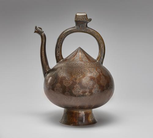 Brass kettle-shaped vessel with a pointed top. The long, upright spout has a roaring dragon head at the tip. The vessel is mounted on a raised, circular base. It has a large, semi-circular handle with a hinged opening at the top. It is decorated with engraved scrolling vine patterns.