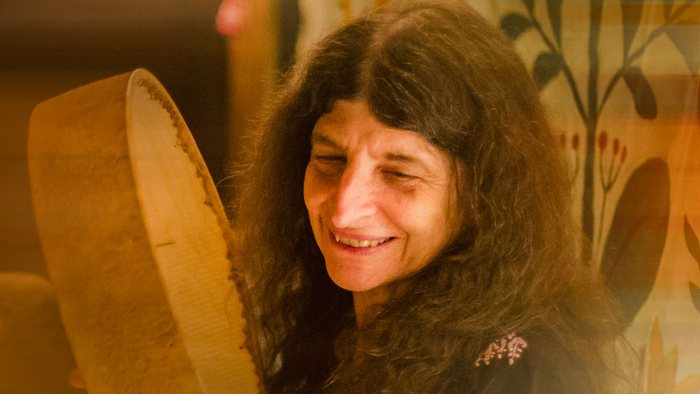 A smiling woman holds up a drum.