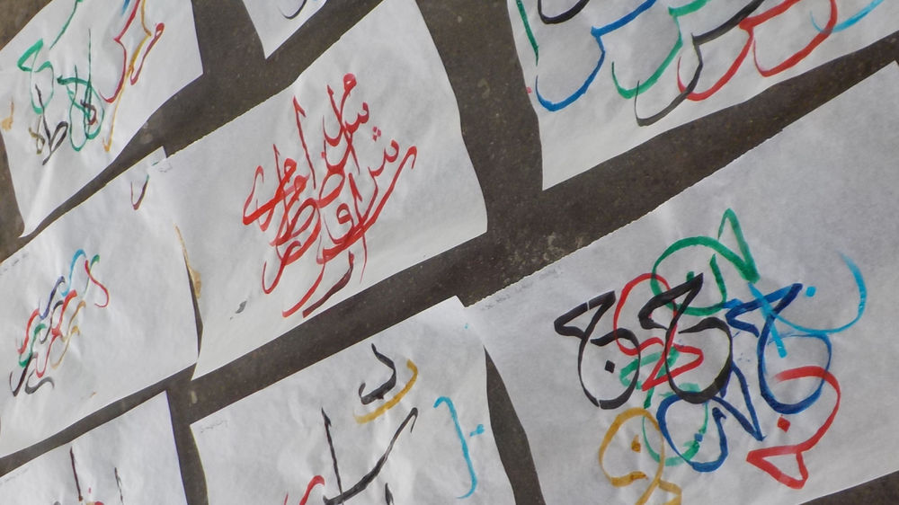 Colourful calligraphic drawings on paper are pinned to a wall.