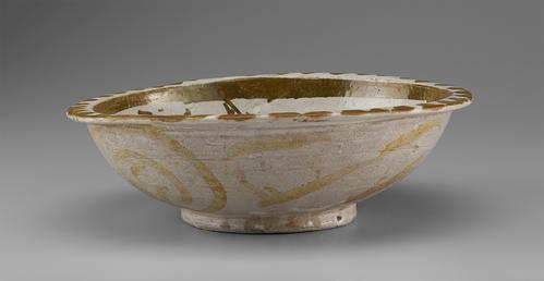 Side view of a circular bowl, decorated in softly metallic gold paint over an off-white base. The flattened rim is decorated in a scalloped pattern. The outside is mostly white, with soft daubs of golden paint. The base is small and slightly raised.