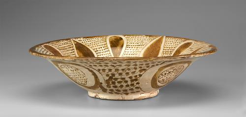 Side view of a cream bowl, decorated with gold paint on a cream background. The base is small and raised. Inside is a pattern of large teardrops, alternating direction, with v-shaped marks filling the spaces. The outside is decorated with four roundels, filled with v-shaped marks, on a dotted background.
