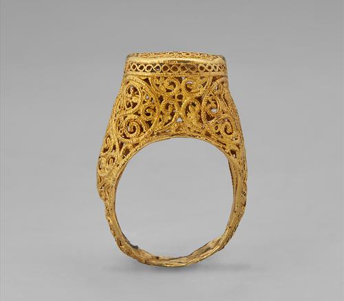 Upright view of a stirrup-shaped ring gold ring with delicate filigree
