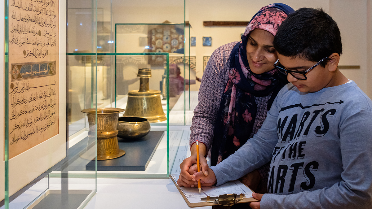 A woman helps guide the hand of a boy who is sketching in front of a folio in the Museum’s permanent gallery.