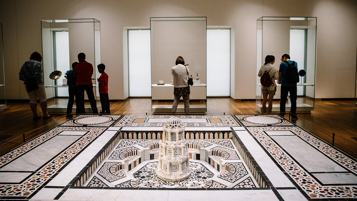 	Several people look into three glass cases in the Museum’s Permanent Gallery, behind a large replica fountain on the floor.