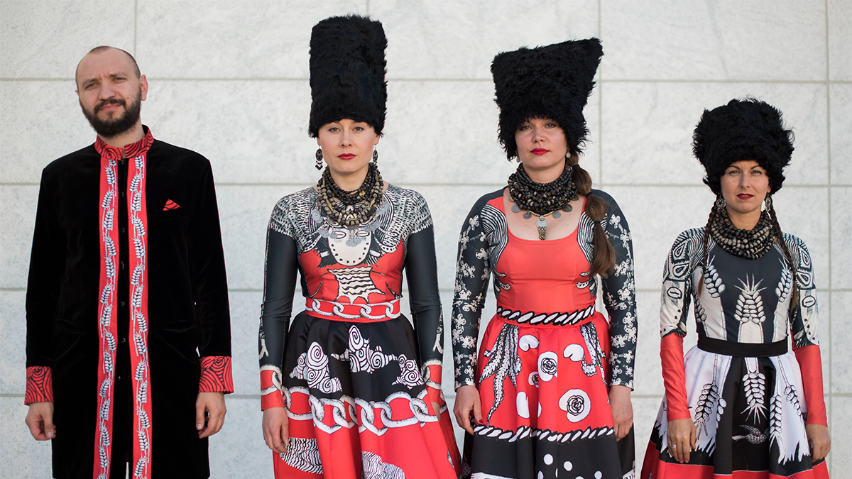 DakhaBrakha’s four members stand outside the Museum, wearing red, black, and white outfits, and tall, woolly black hats.