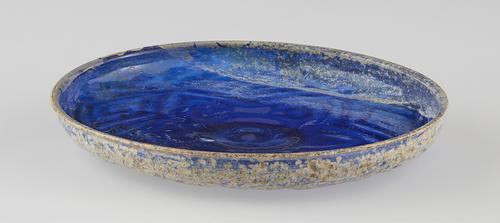 Side of a blue with a shallow wall dish, with beige rim, featuring a narrow everted rim and stands on a ring-like foot.