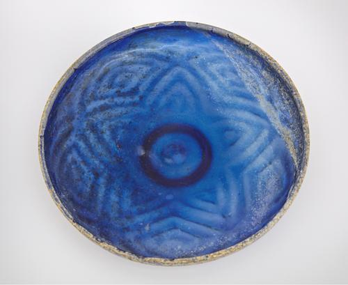 Inside view of a blue with a shallow wall dish decorated with allover pattern. A five-pointed star on its base that continues with a with enclosed triangles up the sides of the walls. 
