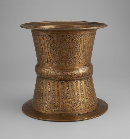 Brass; engraved cylindrical tray stand with silver and gold. A bold Arabic inscription decorates the upper and lower parts of the stand, narrower in the middle at the rib also featuring an Arabic inscription. Large roundel shown on upper part of the stand. 