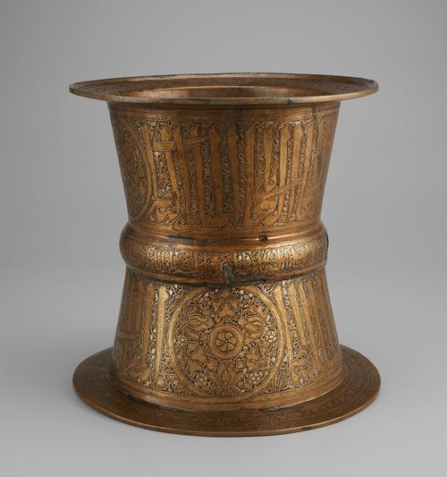 Brass; engraved cylindrical tray stand with silver and gold. A bold Arabic inscription decorates the upper and lower parts of the stand, narrower in the middle at the rib also featuring an Arabic inscription. Large roundel shown on lower part of the stand.