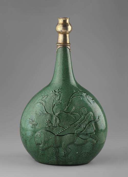 Green bottle, with a flatter sided rounded body rising to a tapering tubular neck with a silver thistle mouth, kick foot underneath. On one side of the bottle, a man struggles to restrain a lion. On the other side, two mythological beasts cavort in a landscape.
