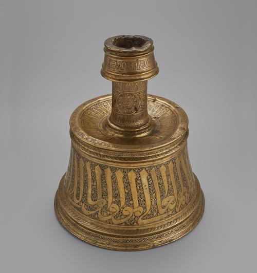 Candlestick with a conical base was hammered from brass sheet in two parts and soldered together, featuring large Arabic inscription on the base, and roundels on the neck.View of the top of the conical base.