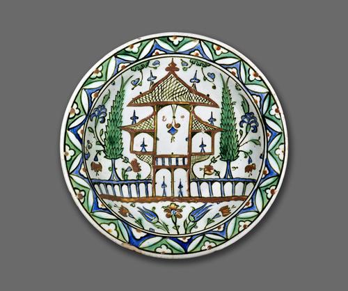 Dish decorated with a two-storied pavilion in a garden of cypress trees, tulips, hyacinths and other flowers. A censer of light hangs from the central arch of the pavilion and candlesticks stand in its other rooms. The rim of the dish is decorated with geometric and floral patterns.   