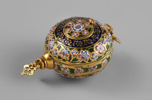 Gold, circular palm sized form, each side with a large and small hinged compartment on each side. Decorated with pink and blue floral pattern and leaves on the outside of the large compartment, and a band of royal blue with flowers on the edge beside of the small compartments on the top.