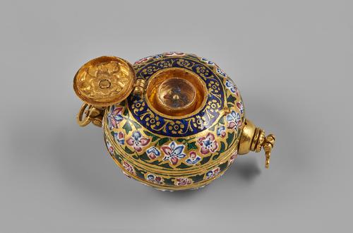 Gold compendium, circular palm sized form. Decorated with pink and blue floral pattern and leaves on the outside of the large compartment, and a band of royal blue with flowers on the top. The small hinged compartment open to view a small compass.