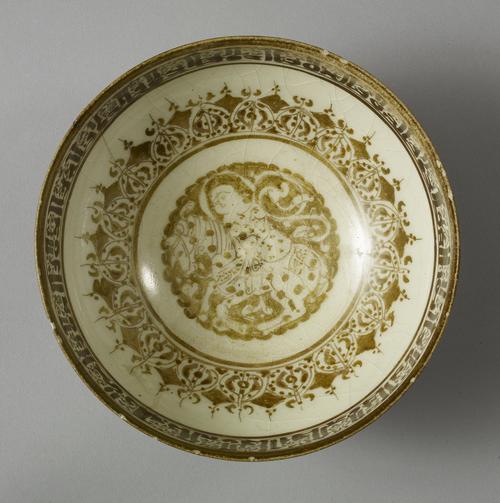 Bowl, golden brown lustre, below the rim on the interior is a band of Kufic script. The central portion of the interior consists of a band of eighteen ovals, each containing foliage which surrounds a medallion of a man on horseback. 
