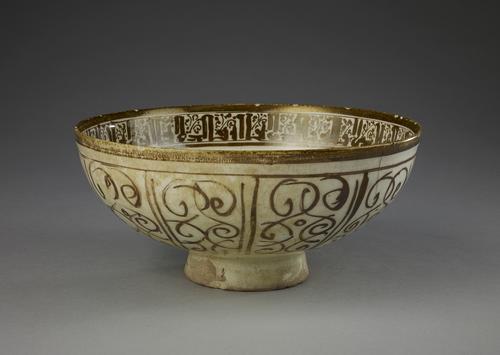 Bowl, golden brown lustre view of  the rim on the interior is a band of Kufic script repeating and the outside walls divided into ten vertical zones, each containing sketchy arabesque foliage.