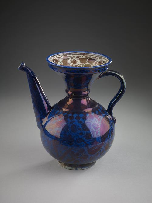 Cobalt pouring vessel with spherical body and wide flaring trumpet mouth. The interior of the flaring top is decorated with brown lustre foliate designs against a white background. On the exterior, brown peacocks and brown foliage, entire surface is covered with dark blue glaze which nearly obscures these underglaze forms.
