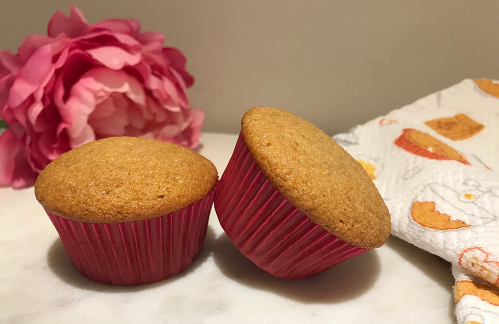 Two muffins in pink paper liners sitting on a table.