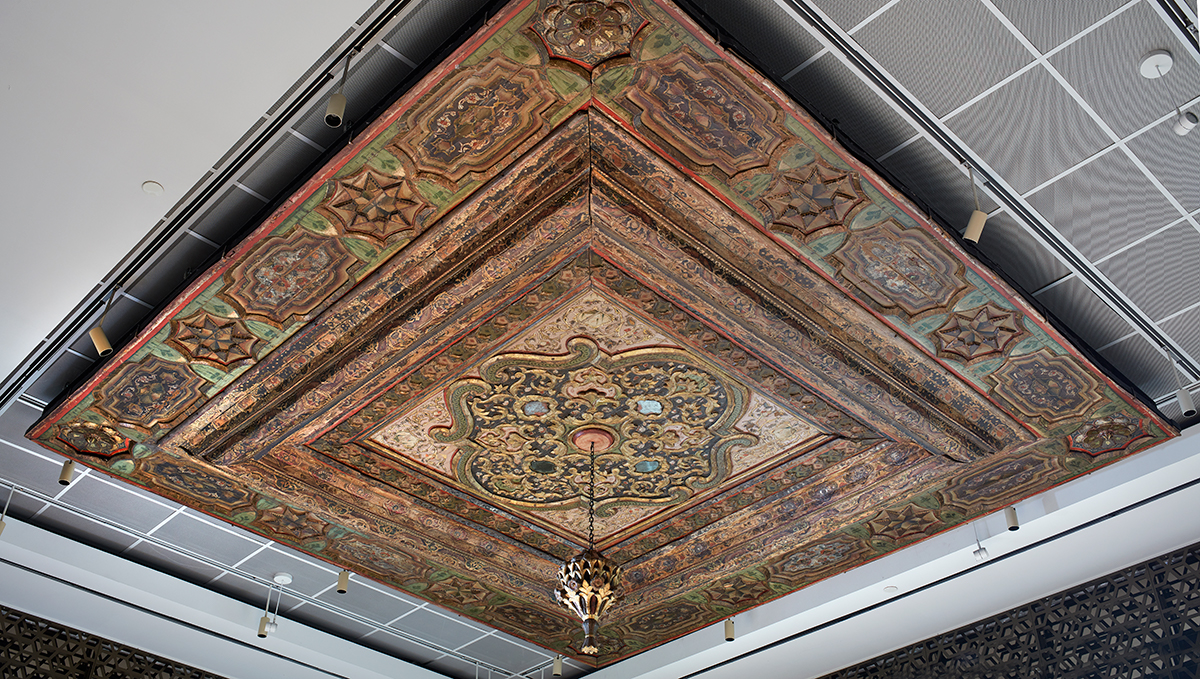 A large ornate ceiling fixture with green, maroon, gold and brown detailing and an elaborate floral design.