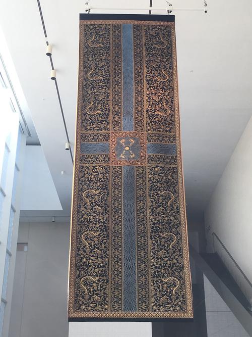 Large carpet, hung from ceiling. Black velvet, with a quadrilateral garden layout, each quadrant contains scenes of wild animals and arabesques forms.They are separated by two intersecting paths in the center.