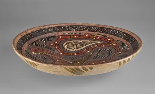 side view of bowl of shallow form, decorated in manganese-brown, tomato-red, white and olive-green slip on a purple ground with the figure of a fabulous bird with palmette wing and calligraphic band around the rim.