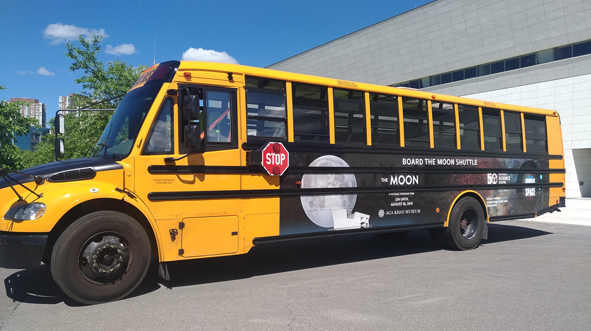 A yellow bus is parked outside in front of the Museum with a Moon shuttle banner on it.