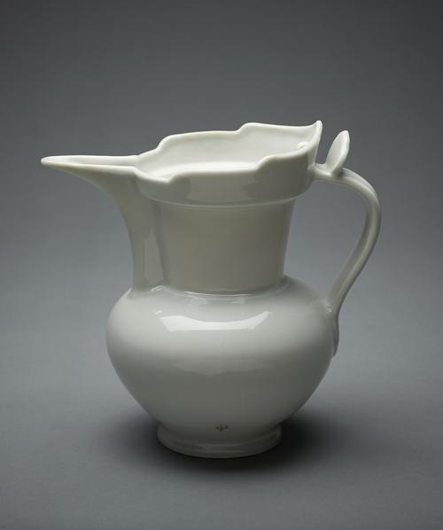 White ceramic jug, with a globular body rising from a splayed foot to a flared cylindrical neck, with a galleried monk’s cap rim with a small lug on the interior, the tall spout of semi-circular section extending the full length of the neck.