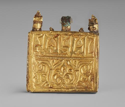 Front of gold amulet qur’an case. Square gold thin box with three loops on the top where it would be hung as a pendant. Inscription and engraving on the front panel.