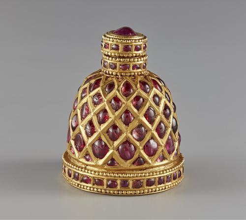 Small jewelled container encrusted with red gemstones. Its top, which is surmounted with a red cabochon stone and surrounded by small gold granules.