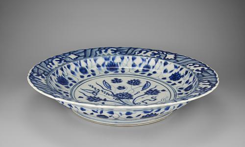 Side view of the blue and white dish that follows a Chinese model so closely that it might have passed for a Chinese original if the body had been translucent like porcelain. Blue and white designs cover the white plate with a foliage design in the centre.