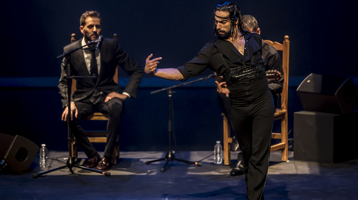 Eduardo Guerreo, all in black, dances furiously on stage with a vocalist sitting in the background