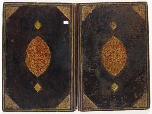Dark brown leather bookbinding laid flat, both sides are mirror images. Golden spiral border, with gold gilt embossed triangular decorative elements on inner corners. Large golden medallion in the centre inlaid with red floral patterns. Spine of the binding has a slight rip.