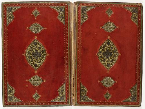 Red leather interior of bookbinding. Delicate golden border with cut-out leather flowers in black on gilt background in the corners. Large central medallion in black on gilt background and pendants in filigree.