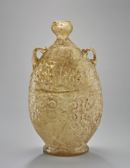 Bottle of flat-sided elongated oval form on spreading kick foot, the constricted neck with spherical mouth, two small applied loop handles on the shoulder, yellow, brown with slight iridescence.