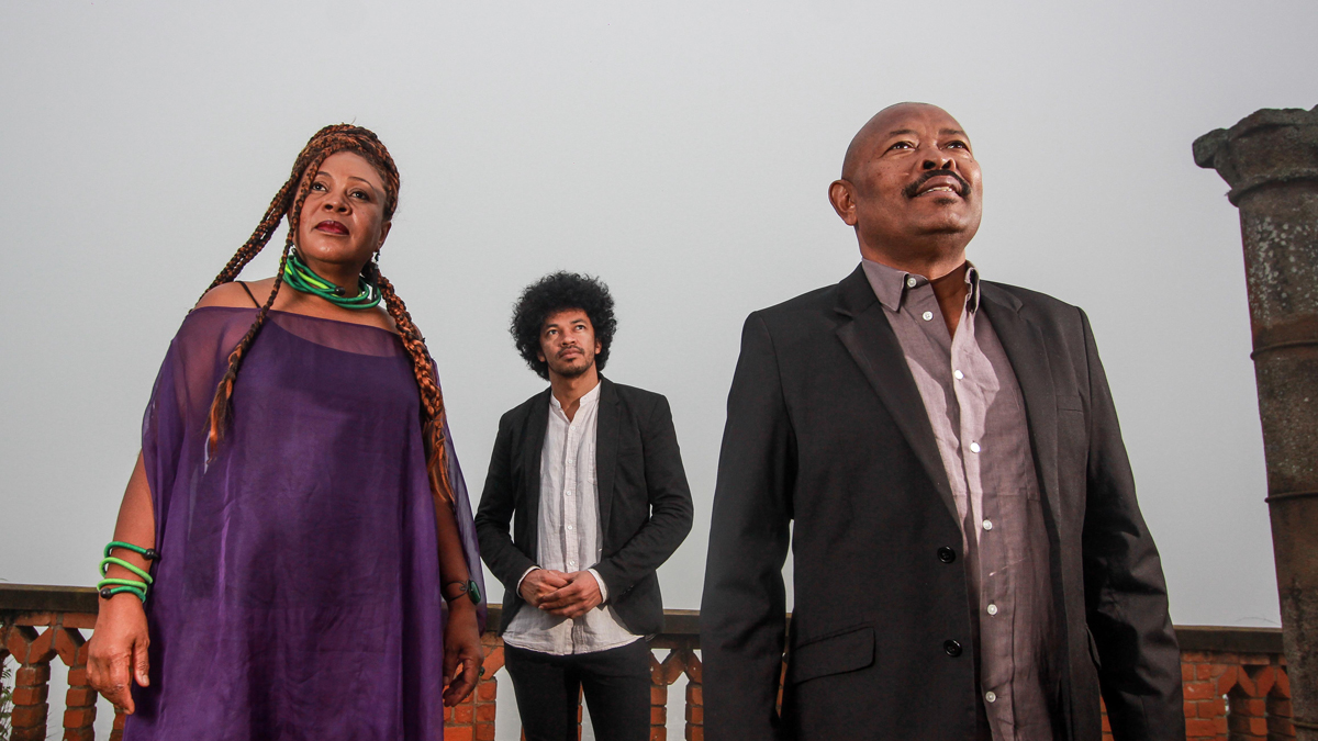 Toko Telo, a trio of Malagasy musicians, stand outside looking upwards.